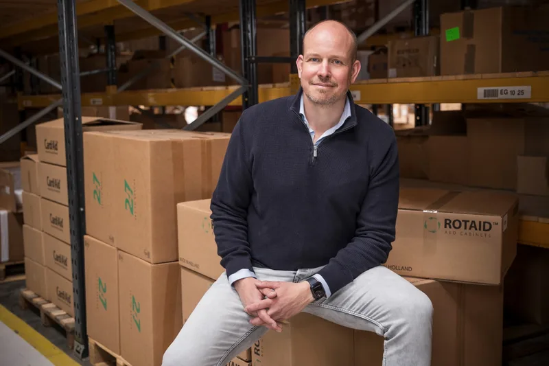 Thomas Balm, eigenaar van AEDCenter, in het magazijn in Hoofddorp tussen dozen met AED's en AED-buitenkasten